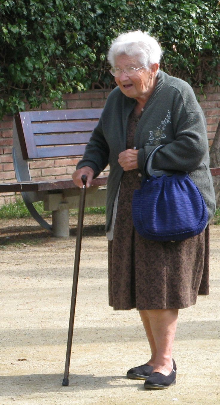 an old woman holding a cane in front of a bench