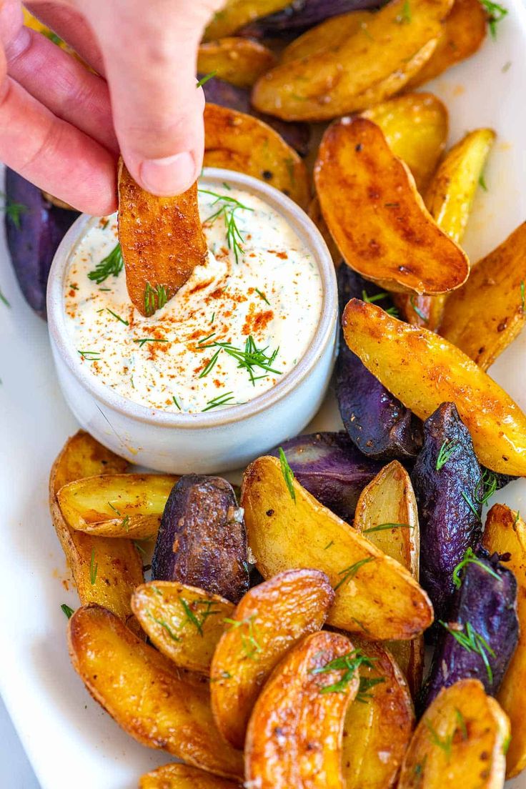 a person dipping some kind of sauce on top of potato wedges in a bowl