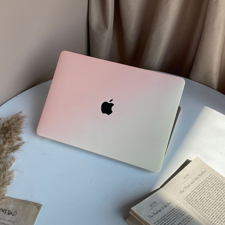 an apple laptop sitting on top of a table next to a book and some feathers