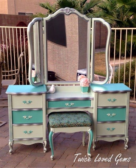 an antique vanity with mirror and stool in front of a fenced area, next to a palm tree