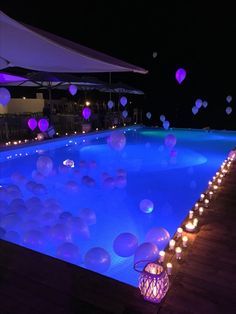 balloons floating in the air over a swimming pool at night with lit candles on the ground