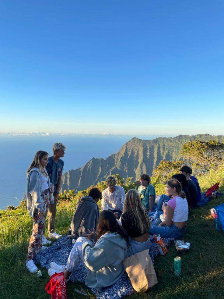 a group of people sitting on top of a lush green hillside next to the ocean