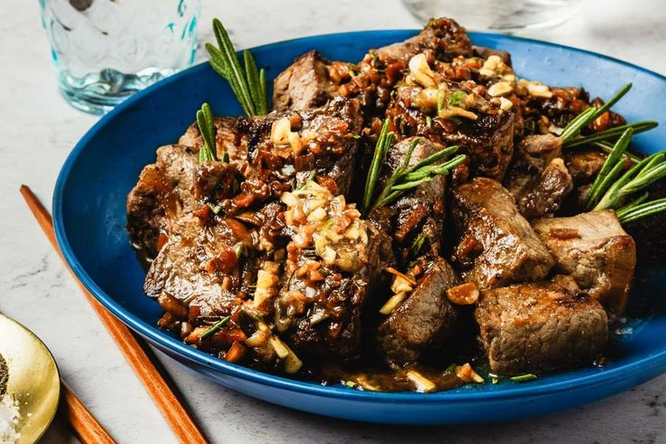 a blue bowl filled with meat and vegetables on top of a table next to chopsticks