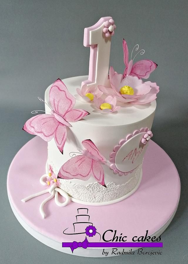 a pink and white cake with butterflies on it's top is decorated with the number one