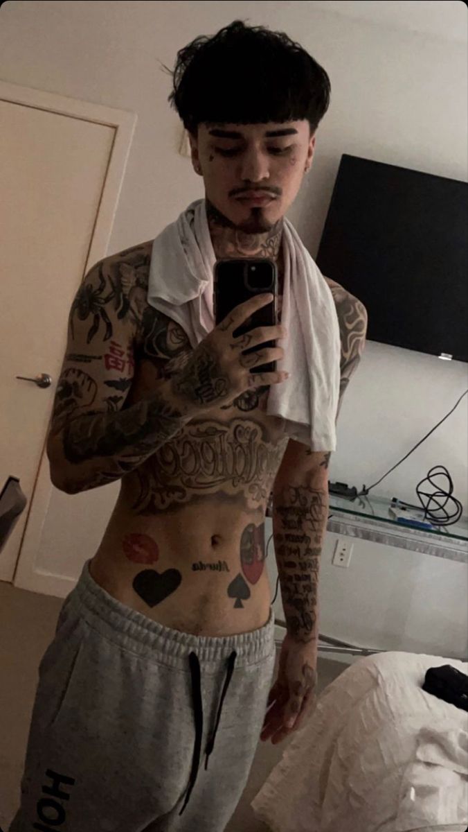 a man with tattoos is taking a selfie in his bedroom while wearing sweatpants