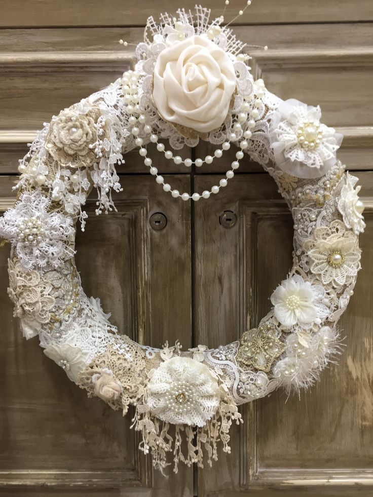 a wreath with flowers and pearls hanging on the front door, decorated with white beads