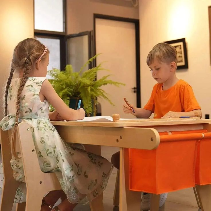 two children are sitting at a table writing