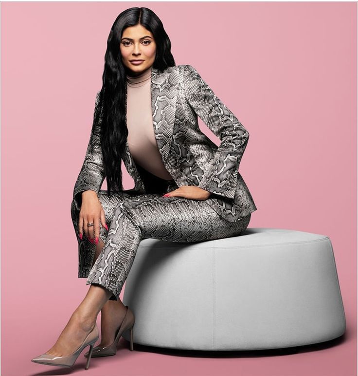 a woman sitting on top of a stool wearing a snake skin suit and high heels