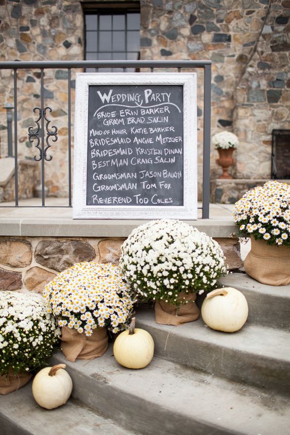 flowers and pumpkins are sitting on the steps in front of a wedding party sign