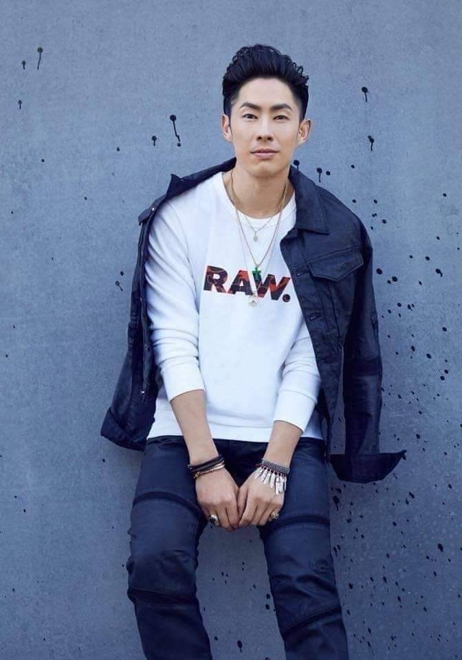 a man sitting on top of a cement wall wearing black pants and a white shirt