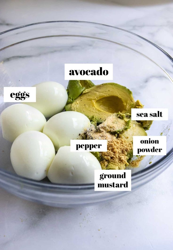 ingredients for avocado in a glass bowl on a marble counter top with labels