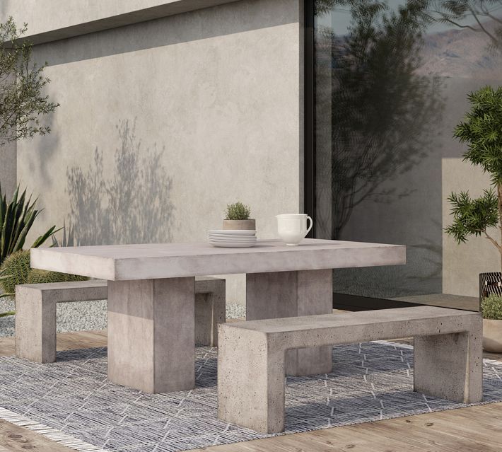 a concrete table and bench in front of a building with potted plants on it