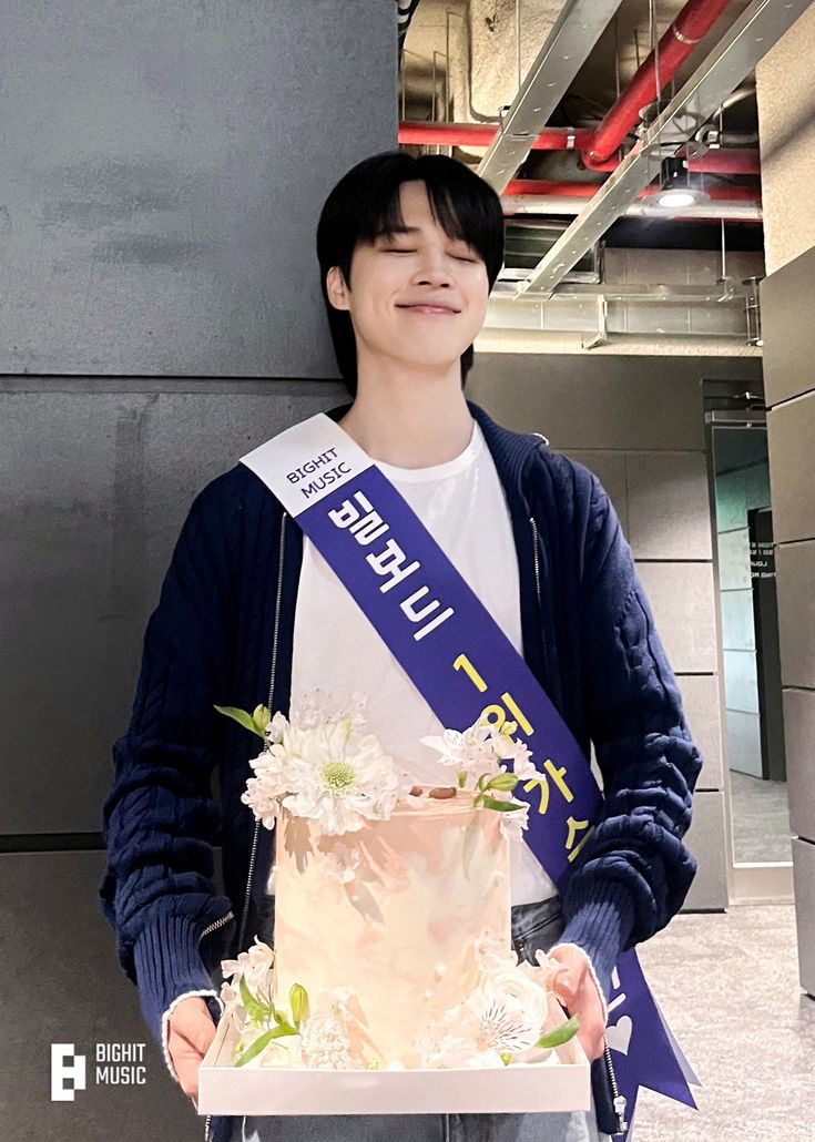 a young man holding a cake with flowers on it in front of a sign that says i love you