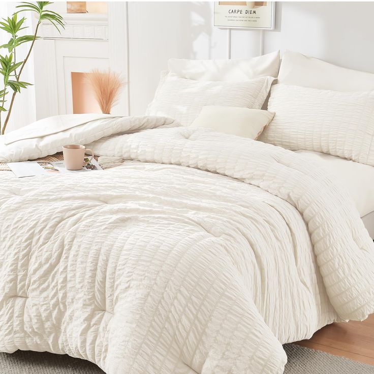 a bed with white comforter and pillows on top of it in front of a potted plant