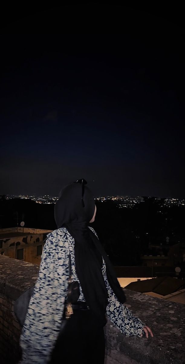 a person standing on top of a roof at night with the city lights in the background