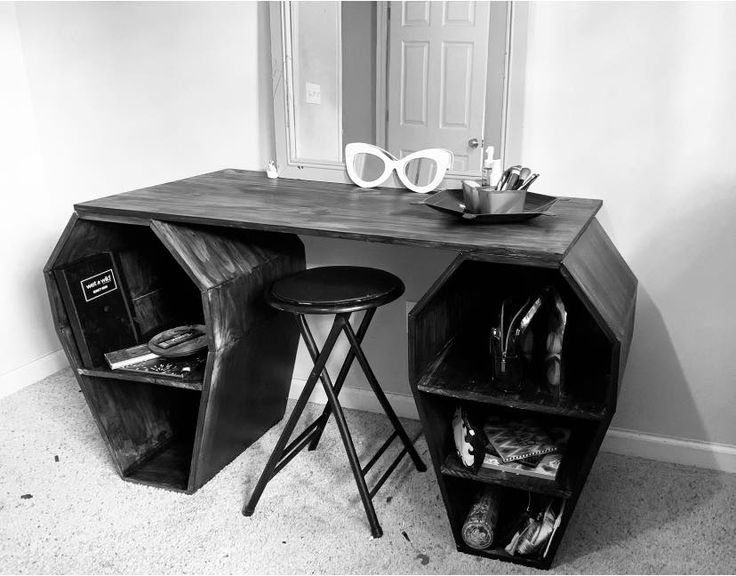 a black and white photo of a desk with two stools next to it on the floor