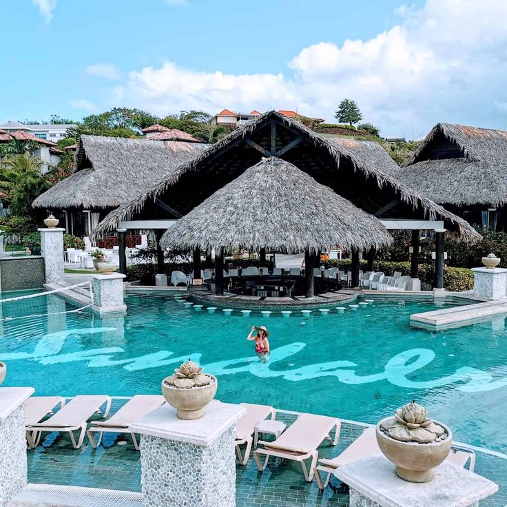 an outdoor swimming pool with lounge chairs and thatched roof huts