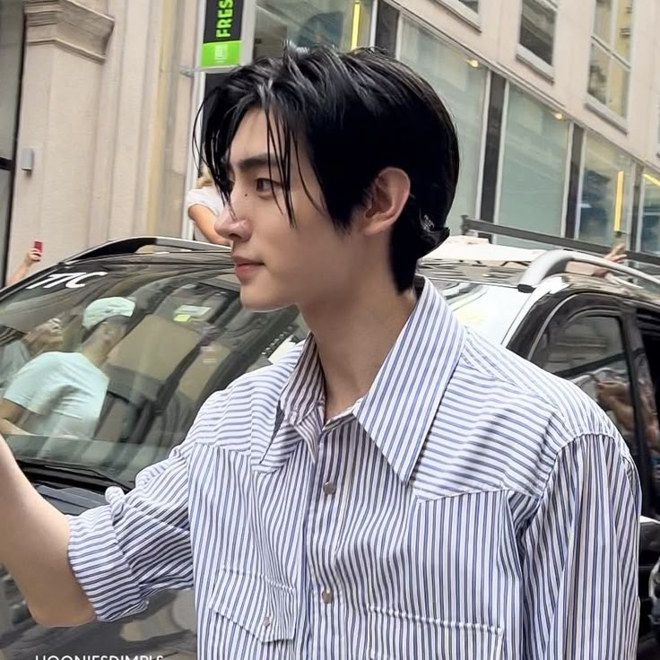 a man with black hair is looking at his cell phone while standing in front of a car