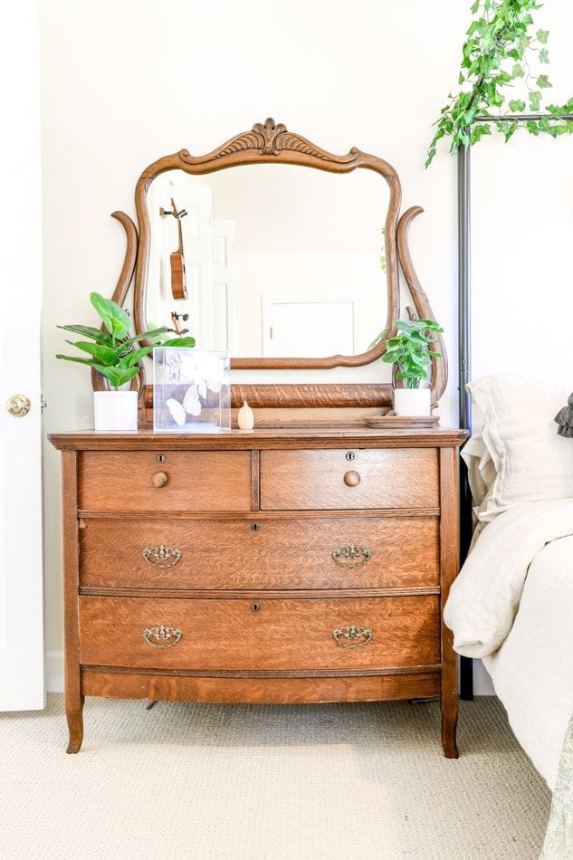 a bedroom with a dresser, mirror and plant on the side table in front of it