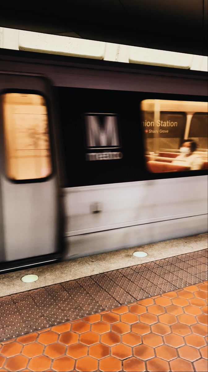 the train is moving fast down the tracks in front of the station platform with its doors open