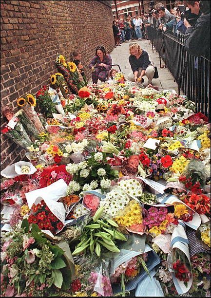 flowers are laid out on the ground in front of a brick wall as people look at them