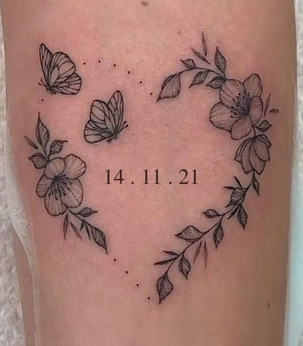 a heart shaped tattoo with flowers and leaves on the side of her leg, which reads date 11 11