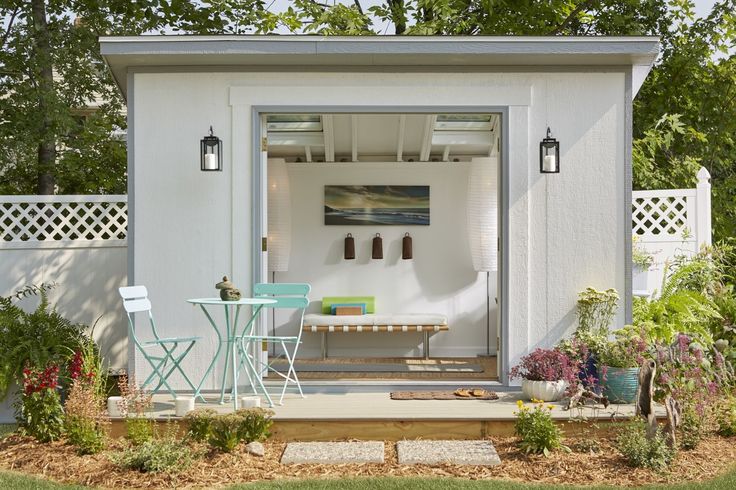 a small white shed with an open door and patio furniture in the front yard area