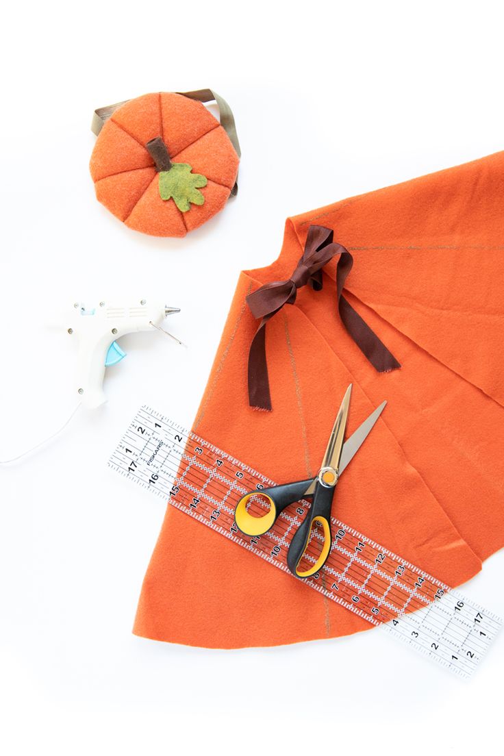 an orange piece of fabric next to scissors and other crafting supplies on a white surface