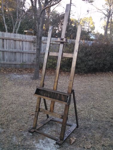 an old wooden easel sitting in the middle of a yard next to a fence