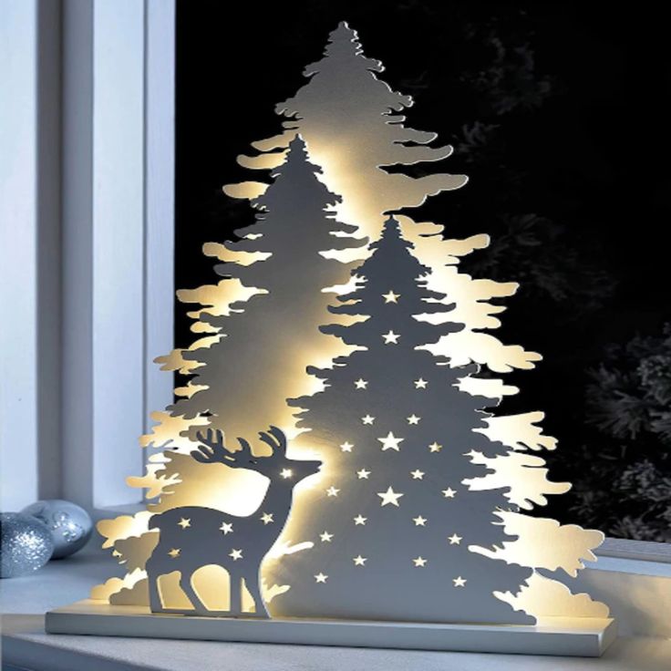 a white christmas tree with lights in the shape of trees and stars on it, next to a window sill