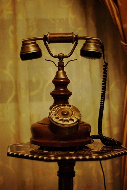 an old fashioned phone sitting on top of a table next to a curtained window