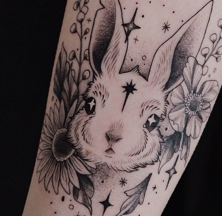 a black and white tattoo of a rabbit with flowers on it's head, surrounded by stars