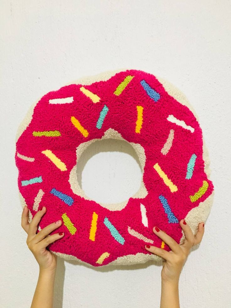 two hands holding up a pink donut pillow with sprinkles