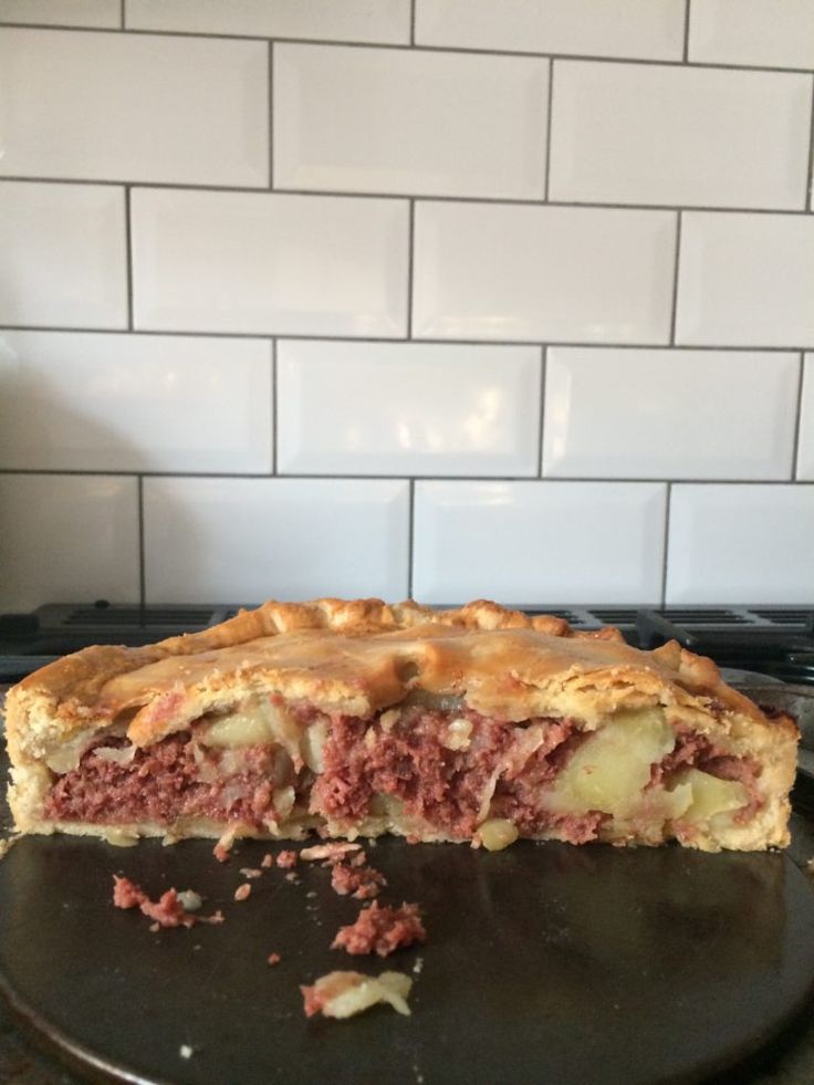 a piece of meat pie sitting on top of a black plate next to a white tile wall