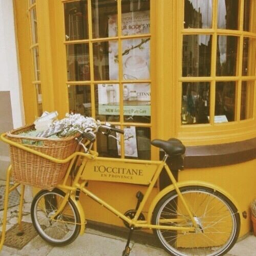 a yellow bicycle is parked in front of a store with large windows and baskets on the back