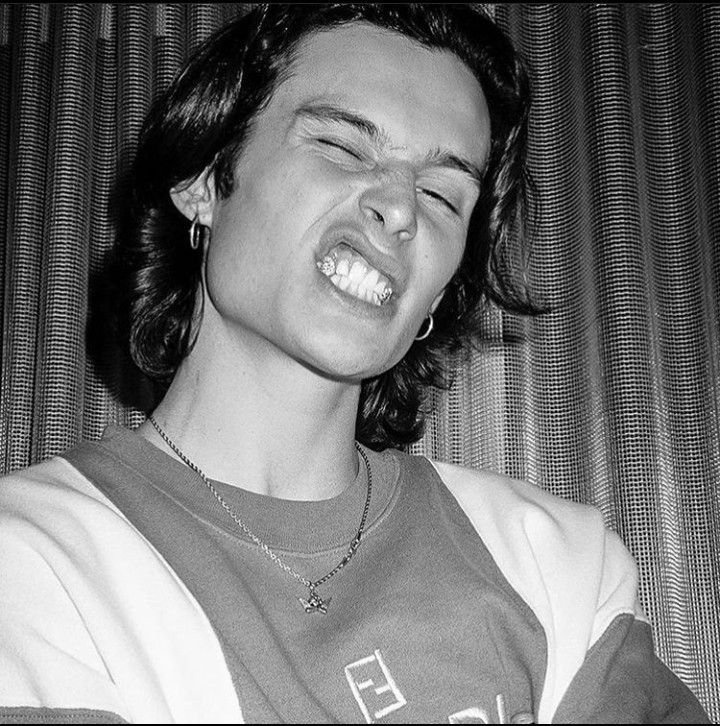 a young man with his eyes closed wearing a necklace and smiling while sitting on a couch