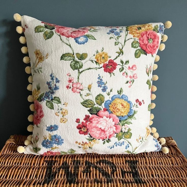 a decorative pillow with pompom trim on it sitting on a wicker basket