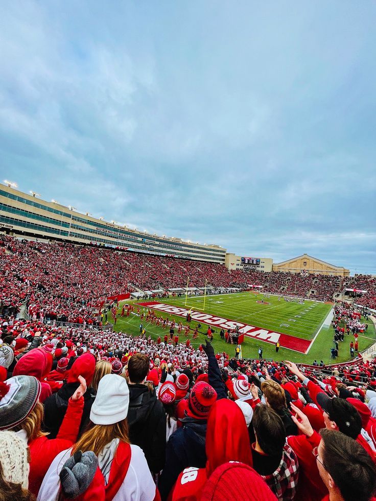 a football stadium filled with people watching a game on the field and fans in red hats