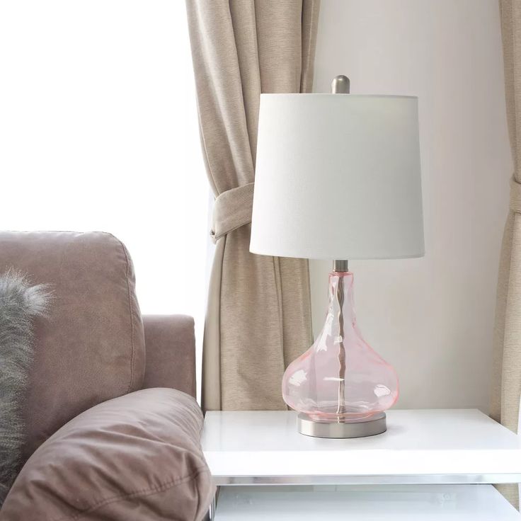 a pink lamp sitting on top of a white table next to a chair and window