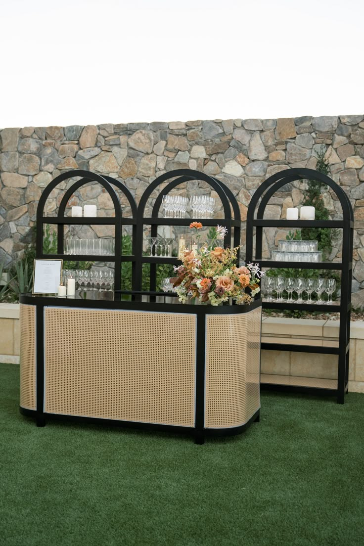 an outdoor bar is set up in front of a stone wall and green grass area