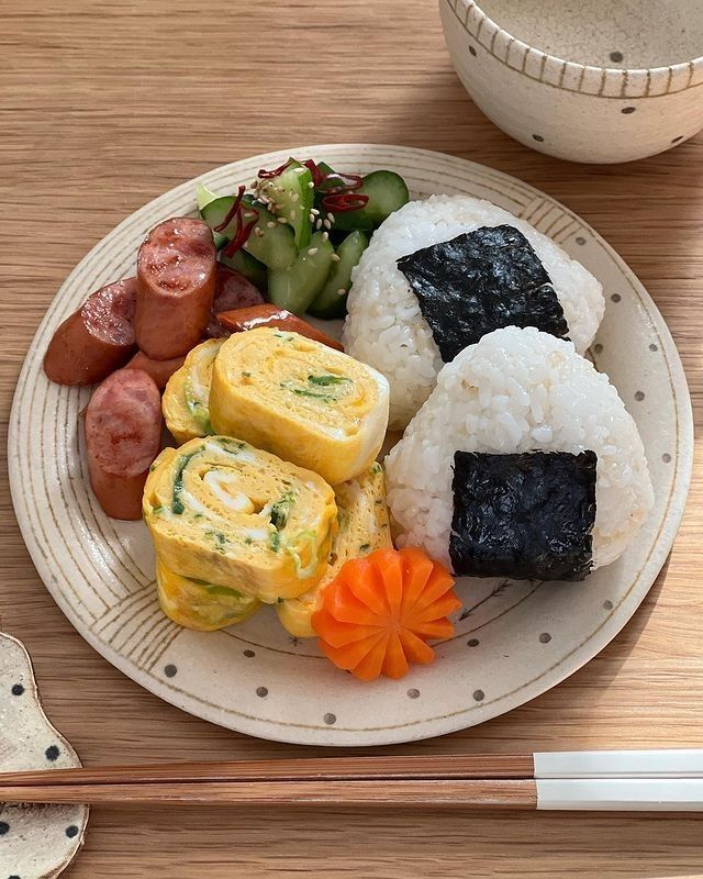 a white plate topped with sushi and vegetables next to chopsticks on a table