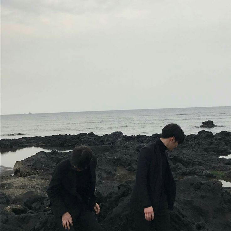 two people sitting on rocks near the ocean