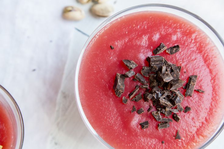 two glasses filled with watermelon, chocolate chips and other food on a table