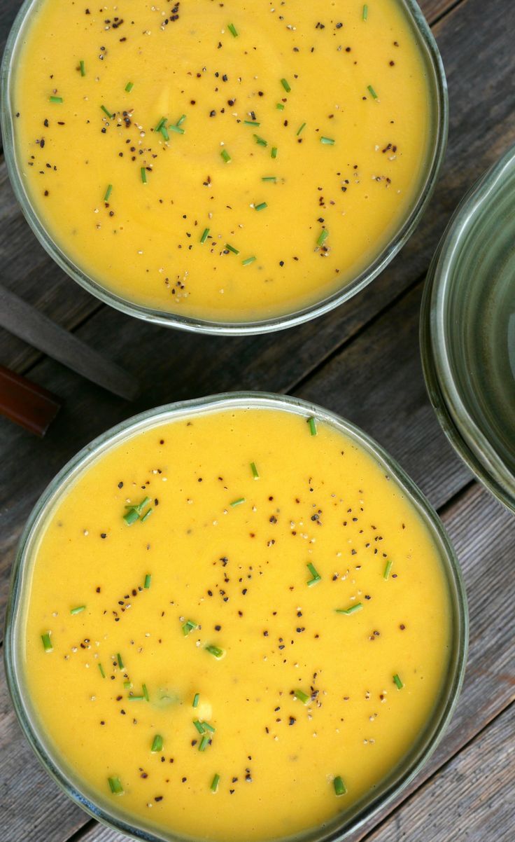 two bowls of carrot parsnip ginger lime soup on top of a wooden table