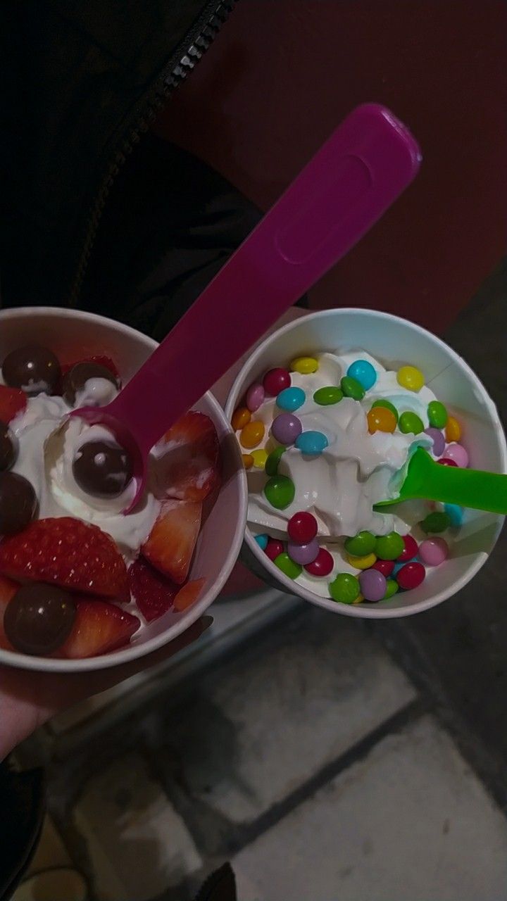 a person holding two bowls filled with ice cream and jelly beans, marshmallows, and chocolate candies