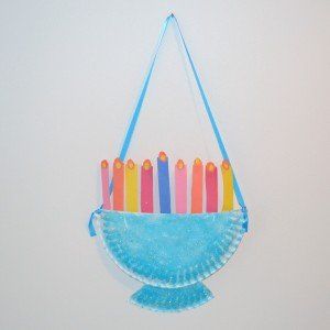 a paper plate with candles on it hanging from a hook in front of a white wall