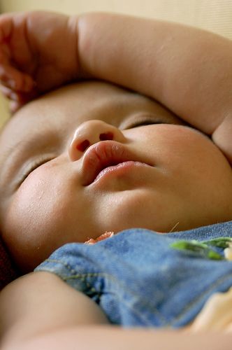 a close up of a baby laying on top of a bed with its eyes closed