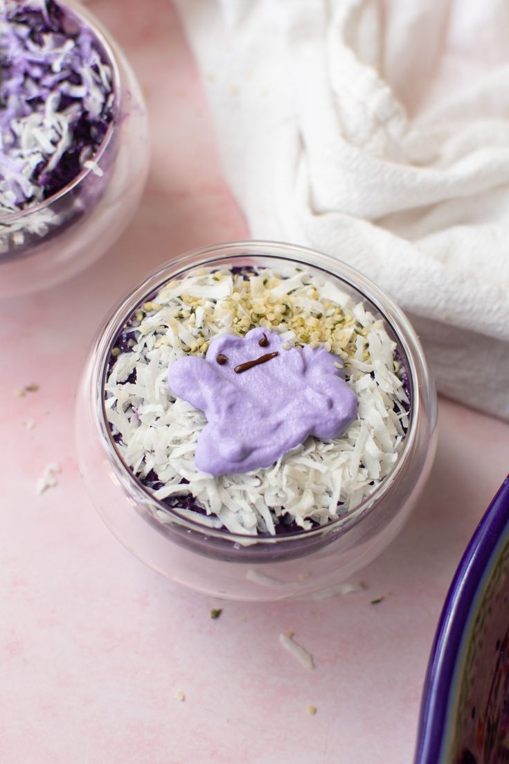 two desserts with purple frosting and sprinkles in small glass bowls