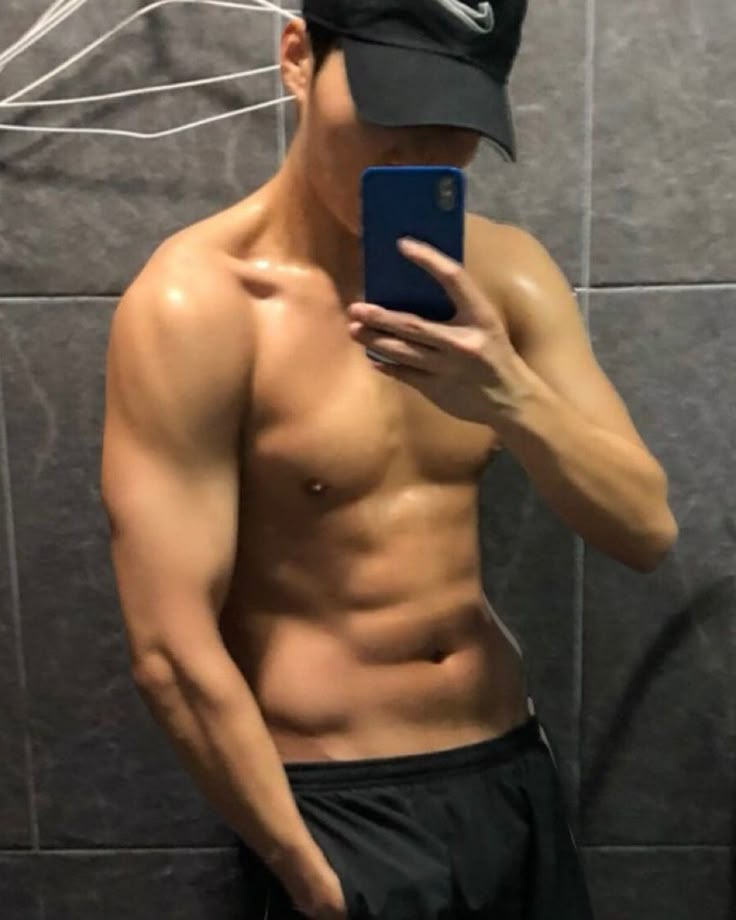 a shirtless man taking a selfie in front of a mirror with his cell phone