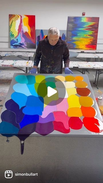 a man standing in front of a table with many different colored paints on it,